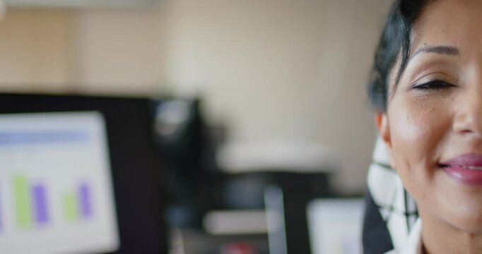 Indian woman watching screen showing bar chart, smiling, eyes closing while at desk, copy space