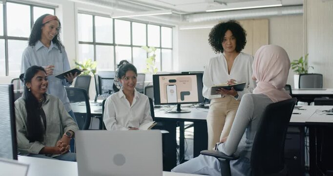 Diverse female coworkers noting on laptops, tablets in office after hijab speaker starting talk