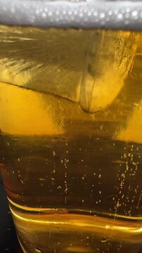 Ice cube falling into foamy golden drink with sparkling bubbles and fizz, dynamic beverage close-up