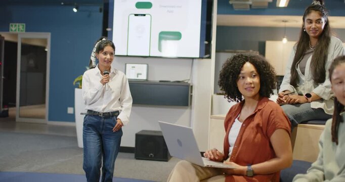 Diverse team watching speaker holding mic showing mockups at work as African woman typing on laptop