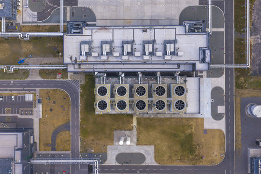 Aerial view of a hyperscale data center with industrial cooling fans and complex piping on the roof, Belgium.