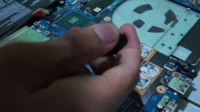 Close-up detailed shot of IT expert applying fresh thermal compound onto laptop CPU processor chip during preventive hardware service and cooling maintenance.