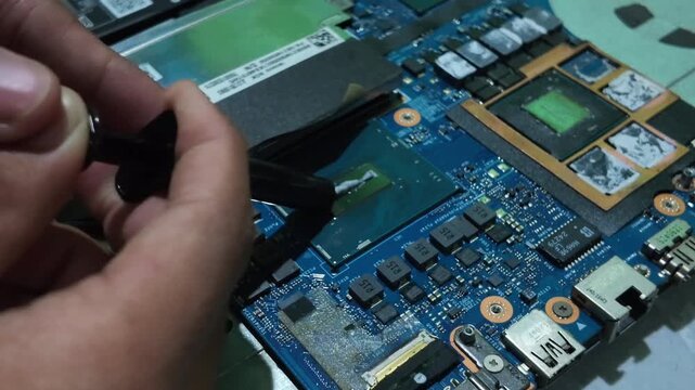 Close-up view of a professional technician performing hardware maintenance, replacing thermal paste on a laptop motherboard CPU to fix overheating issues and boost system cooling performance.