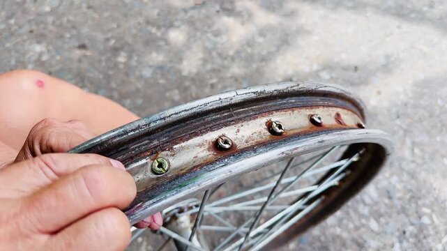 Close-up of a mechanic inspecting a heavily rusted motorcycle wheel rim with spokes outdoors. Concept of vintage bike restoration, wheel repair, worn metal parts, and maintenance work.