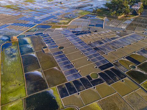 Aerial view of the salt pans on Kutubdia Island, featuring rectangular ponds with varying water levels and colors reflecting the sky, located in Kutubdia, Chittagong Division, Bangladesh.