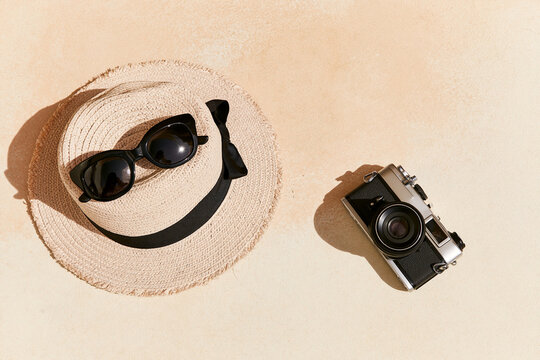 Sunglasses, straw hat and a film camera on sand from above, summer travel flat lay