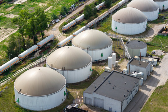 Aerial view of a modern biogas power plant with large dome-shaped digesters and industrial tanks situated near a railway line in Poland.