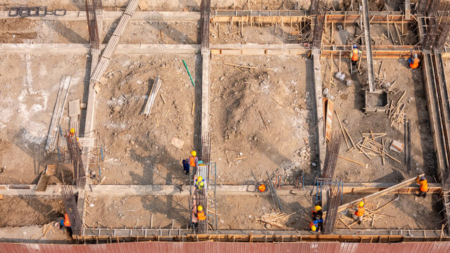 Aerial view of construction workers in safety gear working on the foundation of a building site with rebar, wooden formwork, and piles of earth in Klaten, Central Java, Indonesia.