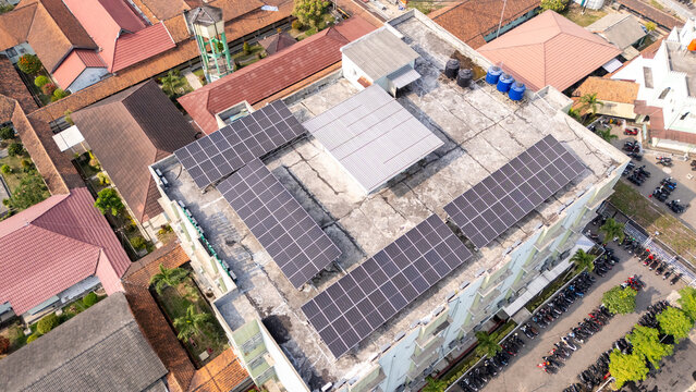 Aerial view of solar panels installed on a building roof with surrounding rooftops and a parking area in Klaten, Central Java, Indonesia.