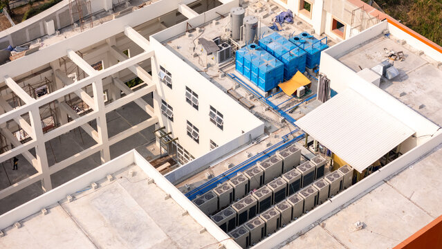 Aerial view of a modern building rooftop featuring rows of HVAC air conditioning units and large blue water storage tanks in Klaten, Central Java, Indonesia.