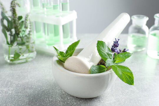 Mortar with pestle, fresh herbs and glassware on grey table, closeup