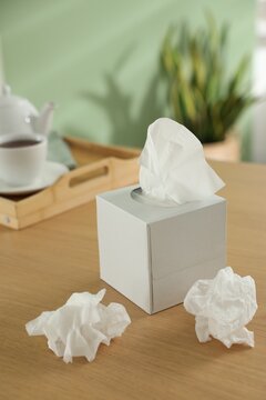 Box of paper tissues and used napkins on wooden table indoors