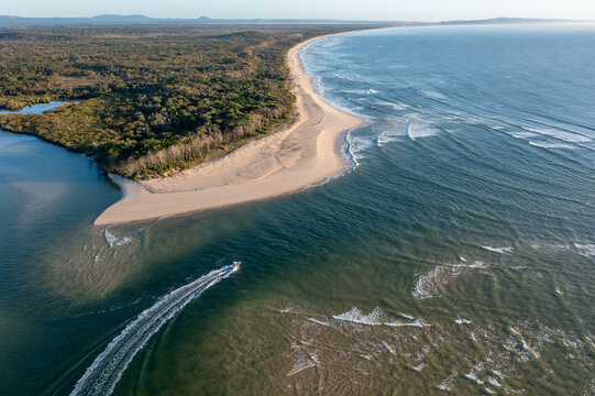 Aerial view of a boat navigating the Noosa River Mouth near a sandy beach and dense forest along the coastline in Noosa Heads, Queensland, Australia.