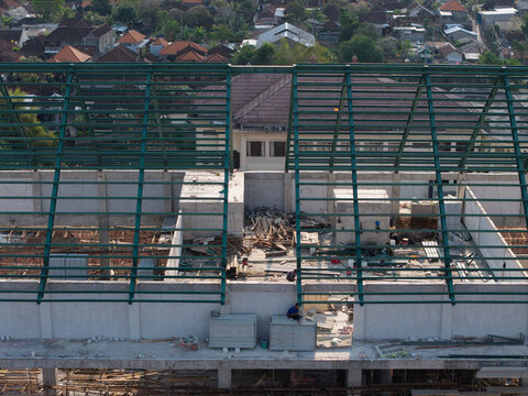 Aerial view of the steel roof framework under construction at the Wangaya Hospital emergency room with workers in the urban landscape of Denpasar Utara, Bali, Indonesia.