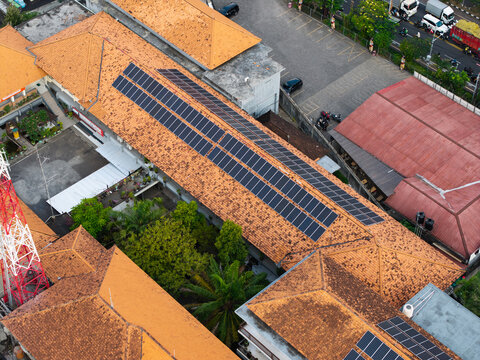 Aerial view of SMKN 1 Denpasar featuring solar panels installed on orange tiled roofs and a lush green courtyard in Kecamatan Denpasar Utara, Bali, Indonesia.