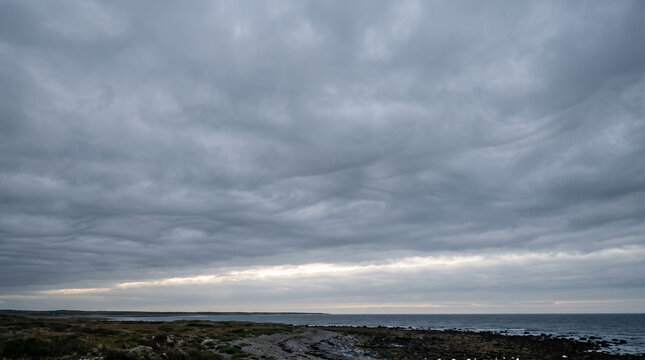 Moody coastal landscape under dramatic overcast sky with dark rolling clouds. Concept of storm clouds, gloomy weather, cloudscape, ocean coast. Copy space.