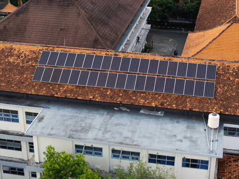 Aerial view of solar panels installed on the tiled roof of the SMKN 1 Denpasar school building in Kecamatan Denpasar Utara, Bali, Indonesia.
