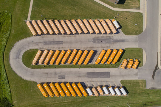 Aerial view of rows of yellow school buses parked in an organized lot surrounded by green grass in the United States.