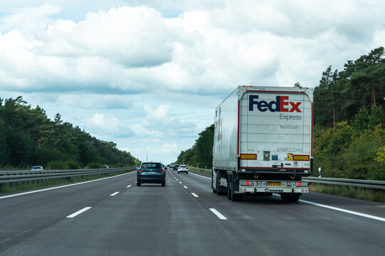 Germany - Aug 22, 2026: FedEx truck overtaken by passenger cars on a three lane German Autobahn with pine forest on both sides, wide shot of highway traffic with a courier lorry under a cloudy summer