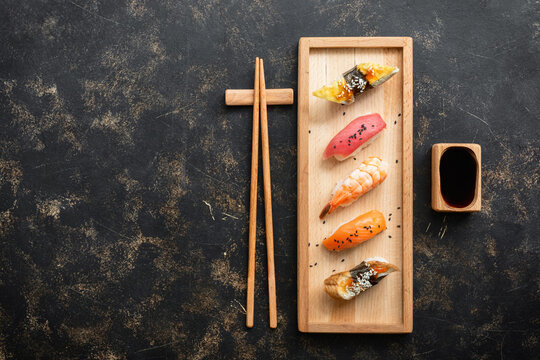 Set of Japanese sushi with soy sauce on a wooden plate with chopsticks, dark rustic background, top view, flat lay, copy space