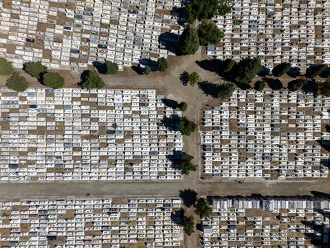 Aerial view of the cemetery with organized rows of white graves, scattered trees, and dirt paths in Evora, Evora District, Portugal.