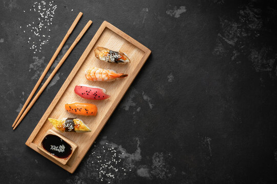 Set of Japanese sushi with soy sauce on a wooden plate with chopsticks, black stone background, top view, flat lay, copy space