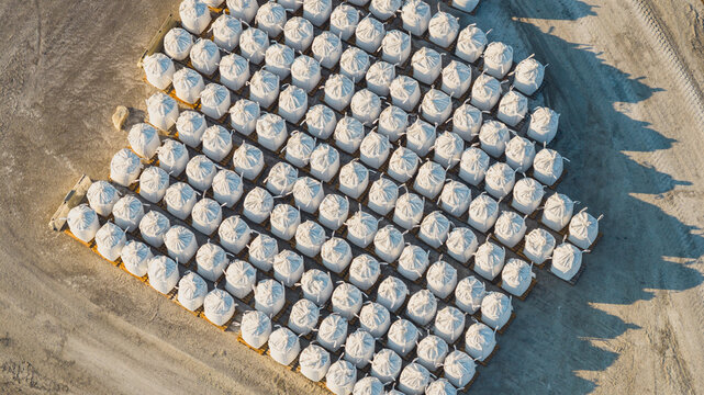 Aerial view of bulk sea salt bags arranged in geometric rows on pallets at an industrial salt production facility in Aigues-Mortes, Occitanie, France.
