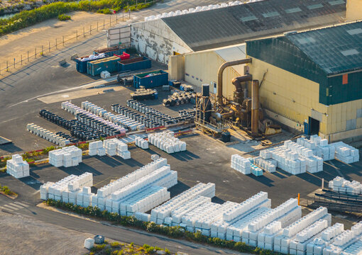 Aerial view of a large sea salt processing and packaging facility with extensive outdoor storage, industrial machinery, and rows of white salt bags, Aigues-Mortes, Occitanie, France.