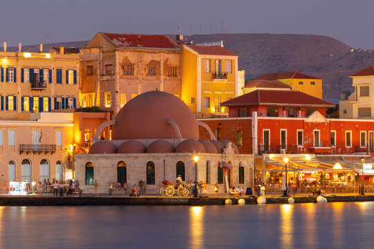 Kucuk Hasan Mosque and historic waterfront buildings illuminated at sunset in Chania, Crete, Greece.