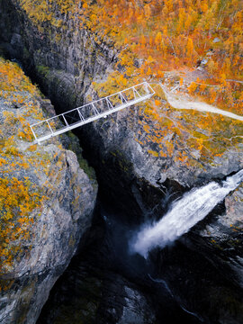 Aerial view of Gorsa bridge spanning a deep canyon with a powerful waterfall and vibrant autumn foliage in Birtavarre, Troms, Norway.