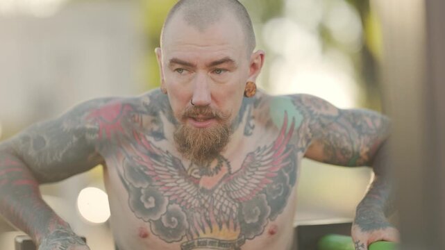 Tattooed muscular man exercising outdoors on parallel bars