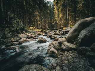 A tranquil mountain landscape featuring a crystal-clear stream winding through rocky terrain and lush greenery. The peaceful flow of water, surrounded by majestic peaks and untouched nature, creates a © molendrach