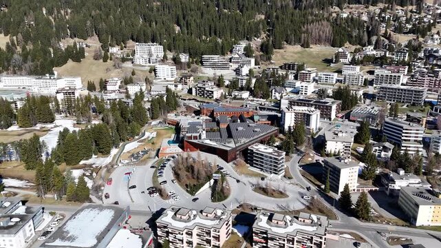 alpine town davos spreads across landwasser valley switzerland congress centre rooftop solar panels catch sunlight snowcapped peaks rise behind forested mountainside graubunden aerial drone footage
