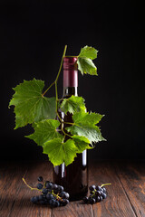 Still life of dark red wine bottle with fresh grape vine leaves and ripe grapes on dark wooden surface © thayra83