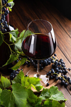 Elegant glass of red wine and bottle surrounded by fresh grapes and leaves on a rustic wooden table