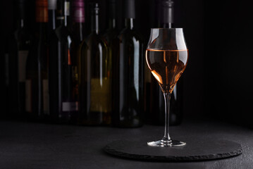 Fototapeta premium Rose wine in elegant glass with bottles in background and dark moody lighting