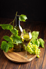 Bottle of white wine with glass and grapes on wooden tray with vine leaves © thayra83