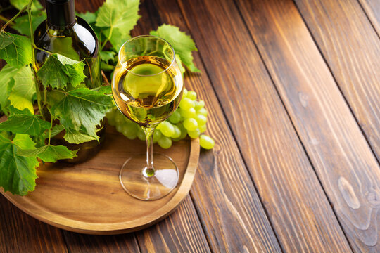 White wine bottle glass and grapes on wooden surface with green leaves for refreshment
