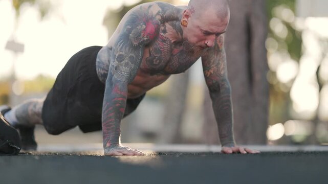Tattooed muscular man doing push-ups outdoor workout
