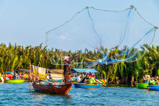A view of a fisherman casting a net on the waterways of the Bay Mau coconut forest in Cam Thanh village near Hoi An, Vietnam on a bright sunny day