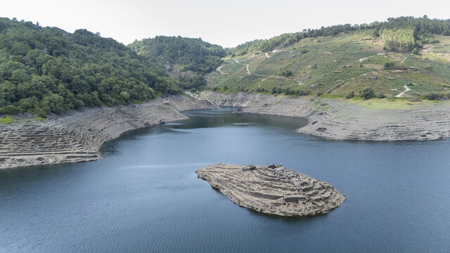 Aerial view of the historic Castro Candaz ruins on a small island in the Mino River, surrounded by terraced hillsides and lush green forests in Belesar, Lugo, Spain.