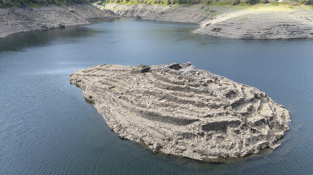 Aerial view of the ancient ruins of Castro Candaz featuring terraced stone walls rising from the reservoir waters in Belesar, Lugo, Spain.
