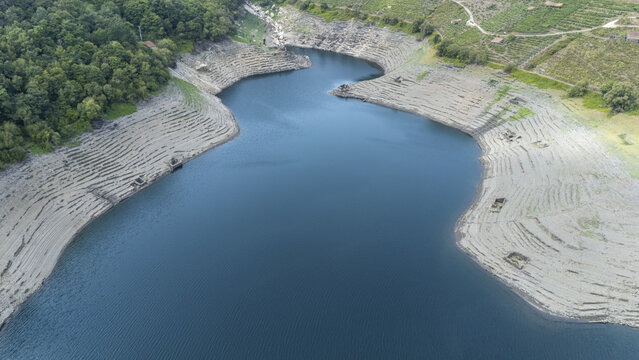 Aerial view of Encoro de Belesar with low water levels revealing terraced banks and surrounding hills in Lugo, Lugo, Spain.