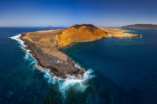 Aerial view of the volcanic landscape of Playa de la Cocina on La Graciosa island, featuring a striking yellow crater, rugged rocky coastline, and turquoise waters in the Canary Islands, Spain.