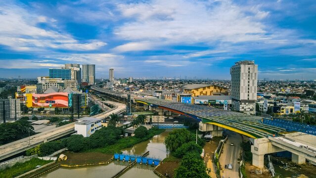 Aerial view of the urban landscape of Bekasi Barat, featuring elevated highway infrastructure, modern buildings, a river, and lush greenery in Bekasi Barat, West Java, Indonesia.