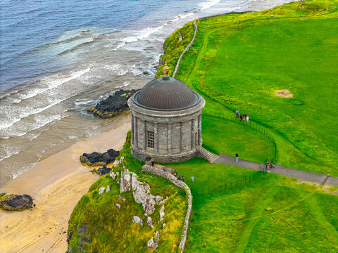 Aerial view of Mussenden Temple perched on the cliff edge above Downhill Strand, surrounded by lush green grass and the Atlantic Ocean in Coleraine, Causeway Coast and Glens, United Kingdom.