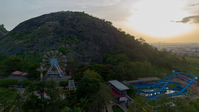 Aerial view of Magic Land amusement park featuring a Ferris wheel and water slides nestled at the base of a large hill during sunset in Kunkwaba, Federal Capital Territory, Nigeria.