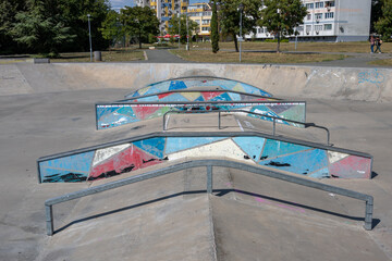 A spine ramp with metal grind rails and colorful geometric street art stands ready for tricks at an urban outdoor skatepark. © Andrey