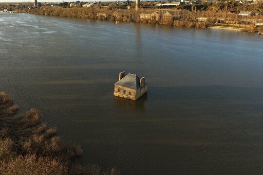 Coueron, France - 29 December 2025: Aerial view of La Maison dans la Loire, a house-like sculpture partially submerged in the river with calm water and the riverbank in the background.