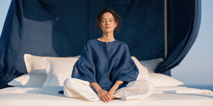Woman in a relaxed seated pose on a layered pillow bed with navy canopy for meditation banner and lifestyle background